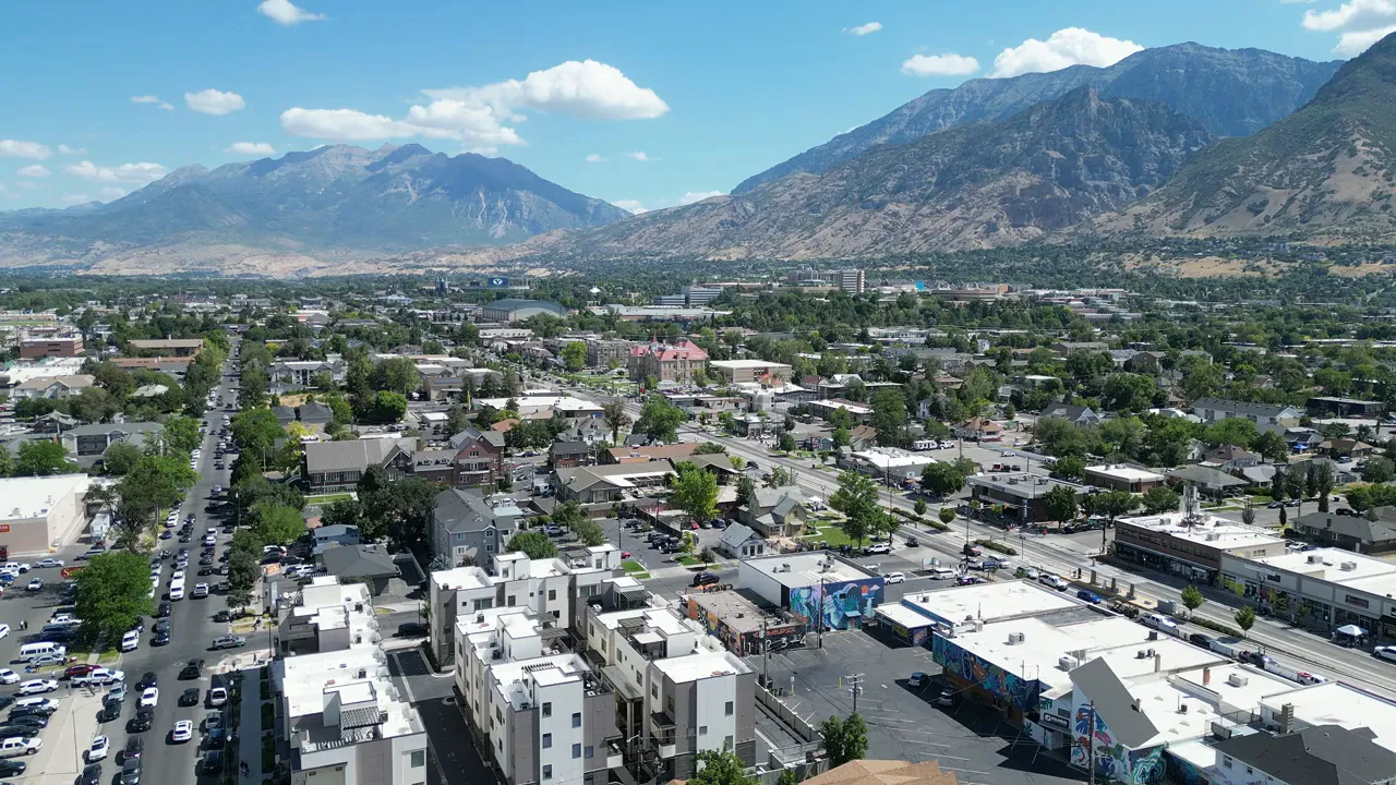 Wide aerial of a Utah Valley neighborhood with mountains behind and retail clusters visible