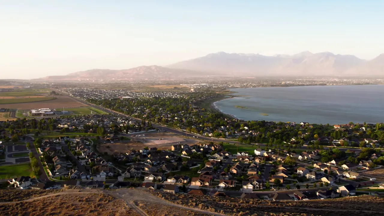 Aerial shot of Wasatch Front suburbs along a shoreline with mountains in the distance